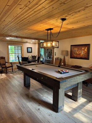 A pool table in a room with wooden flooring and a ceiling with exposed beams.