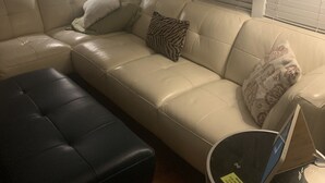 A living room with a beige sofa, a black ottoman, and a lamp. - Cozy 3 bedroom house , pet friendly , yard (Portsmouth)
