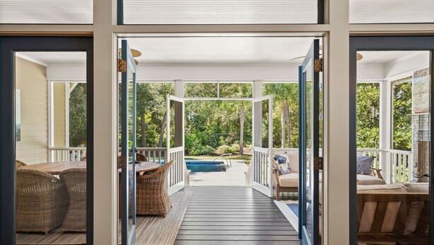 Um deck de madeira leva a uma piscina com móveis de vime e vista para um jardim exuberante.