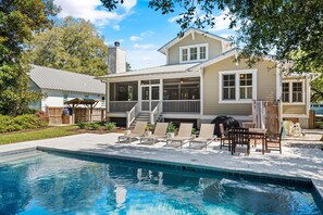 A poolside area with a covered patio, lounge chairs, and a barbecue grill.