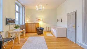 Ein helles Zimmer mit Esstisch, Stuhl, Bett und einer Chandelier.