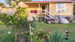 A house with a porch, a motorcycle, and a garden with hydrangeas and other flowers. - 2 bedroom cozy home in Ramdala (Ramdala)