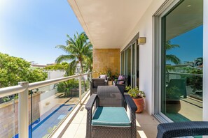 Un balcon agrémenté de meubles en osier, d’une plante en pot et offrant une vue sur des palmiers et des immeubles.
