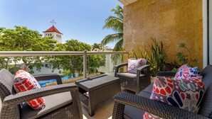 A balcony with wicker furniture, a view of a church, and tropical plants.