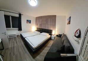 Et hotelværelse med en dobbeltseng, en sofa, et sengebord med lampe, en radiator og et vindue med gardiner.