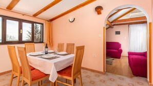 Een eethoek met een tafel voor vier personen, houten stoelen, een raam met gordijnen en uitzicht op buiten.