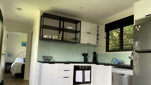 A modern kitchen with white cabinetry, a stainless steel refrigerator, and a window with blinds.