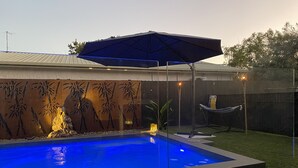 A swimming pool with a bamboo-themed wall, a hammock, and a tiki torch.