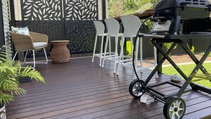 An outdoor patio with a grill, white chairs, and a wicker chair.