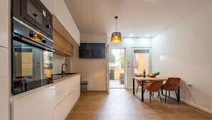 Een moderne keuken met een ingebouwde oven, een eethoek met tafel en stoelen, en uitzicht op de achtertuin.