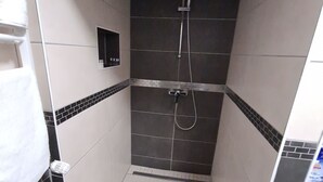 Un petit espace de douche carrelé, équipé d’un pommeau de douche à main et d’un robinet fixé au mur.