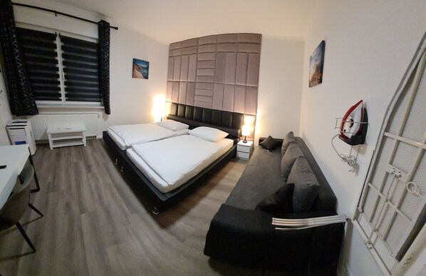 A hotel room with a bed, a sofa, a desk, and a radiator. - W5 Apartment with 2 Bedrooms (Hüllhorst)