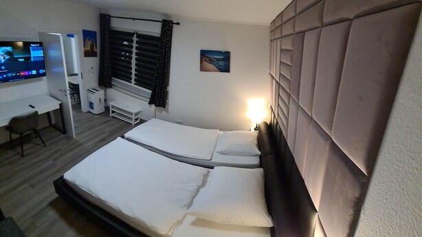 Une chambre d’hôtel avec un grand lit, un bureau avec un ordinateur, une fenêtre avec des stores et un téléviseur fixé au mur.