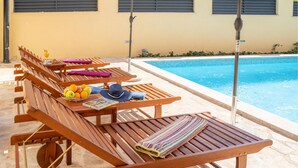 A poolside area with wooden loungers, a table with fruits and a magazine, and a pool. - Cozy apartment in Zadar with WiFi (Zadar)