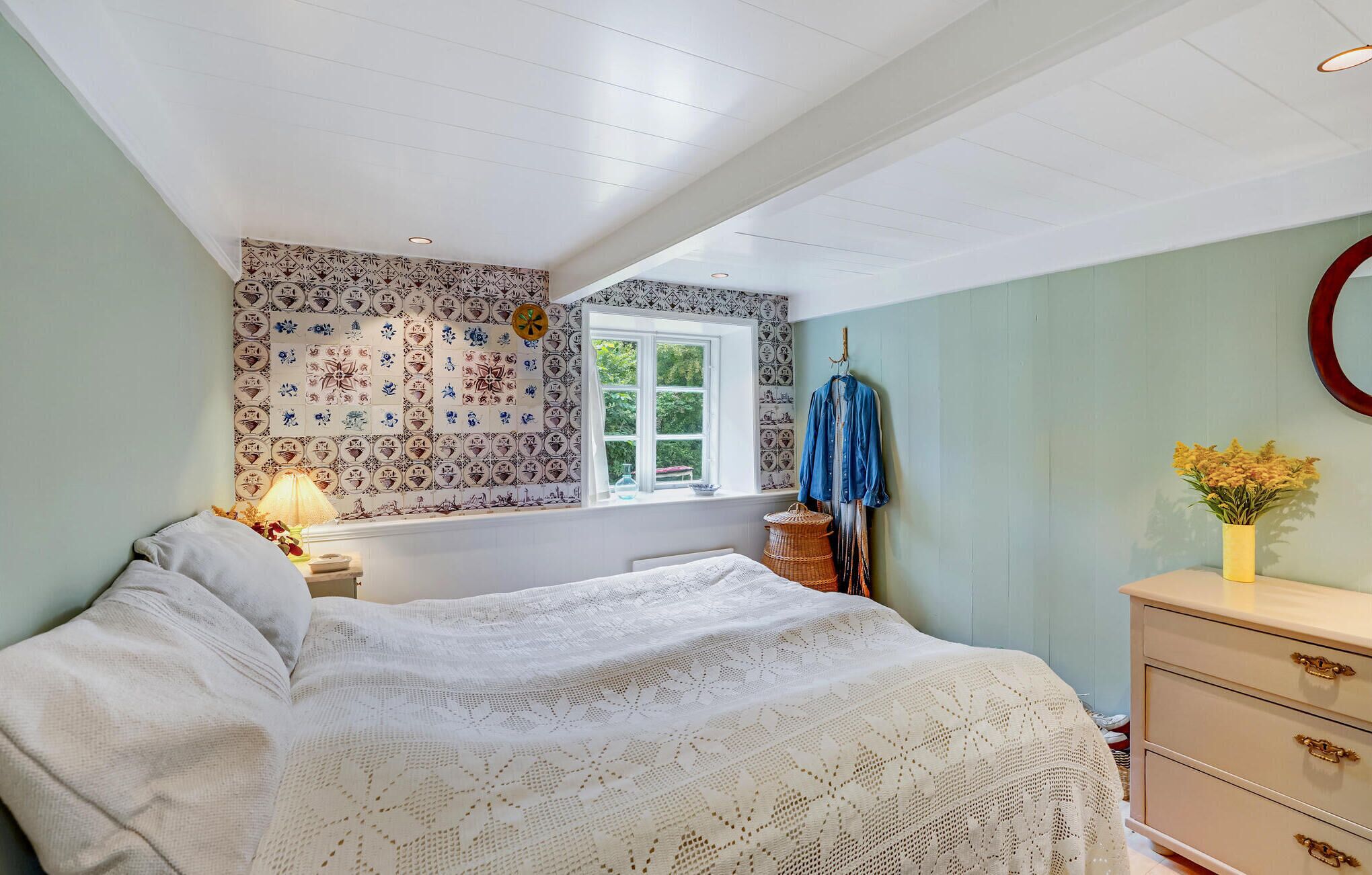 A bedroom with a bed, a window, a dresser, and a wall with patterned tiles.