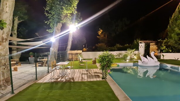 Un espacio exterior bien iluminado con piscina, césped verde y un pequeño pabellón.
