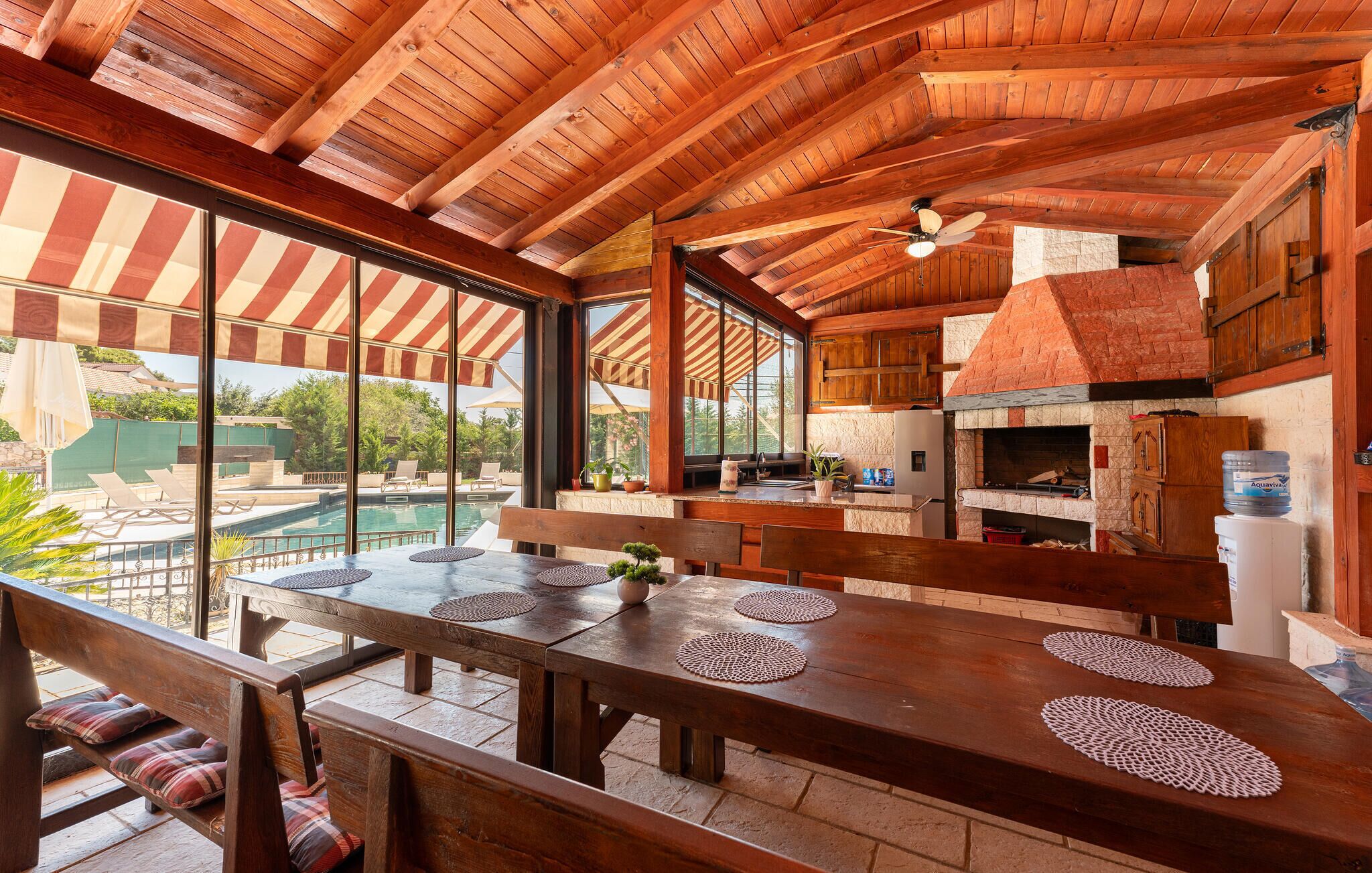 Comedor de madera con vistas a una piscina, chimenea de ladrillo y ventilador de techo.