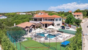 Ein Wohnhaus mit Schwimmbad, Tennisplatz und überdachter Terrasse.