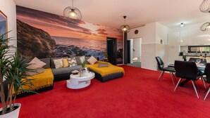 Ein Wohnzimmer mit rotem Teppich, einer Sofagarnitur, einem Couchtisch und einem Essbereich mit Stühlen.