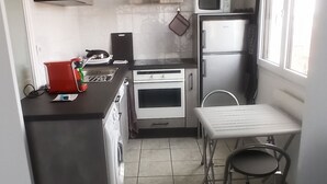 A compact kitchen with a washing machine, a microwave, a refrigerator, and a dining area with a table and chair. - APPRENTICE AMBILLY (Ambilly)