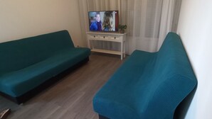 A living room with a teal sofa, a white side table, and a television. - APPRENTICE AMBILLY (Ambilly)