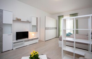 A modern hotel room with a flat-screen TV, a bedside table with a lamp, a wardrobe, a bunk bed, and a small plant on a table. - 2 bedroom awesome apartment in Rabac (Rabac)