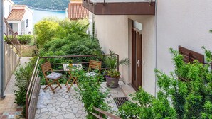 Ein Balkon mit Steinboden, zwei Holzstühlen, einem kleinen Tisch und einem Blumentopf.