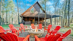 Une cabane avec un foyer et des chaises Adirondack rouges, située dans un cadre forestier.