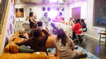 A group of people seated on a sofa in a room with a kitchen area in the background.