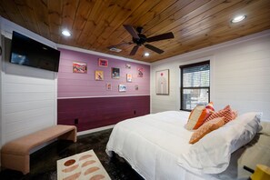 Une chambre avec un plafond en bois, un lit avec une literie blanche, un banc et un mur orné de tableaux.