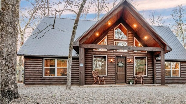 Une cabane en rondins avec un toit à pignon, de grandes fenêtres et une véranda équipée de fauteuils à bascule.