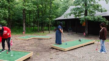 A mini-golf course set up in a wooded area with wooden platforms and a small building in the background.