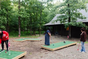 Un parcours de mini-golf aménagé dans un espace boisé, avec des plateformes en bois et un petit bâtiment en arrière-plan.