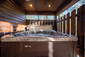 Un bain à remous dans un chalet en bois, avec une clôture en bois et des arbres en arrière-plan.