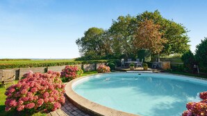Uma piscina com deck de madeira, rodeada por vegetação exuberante e uma grande árvore.