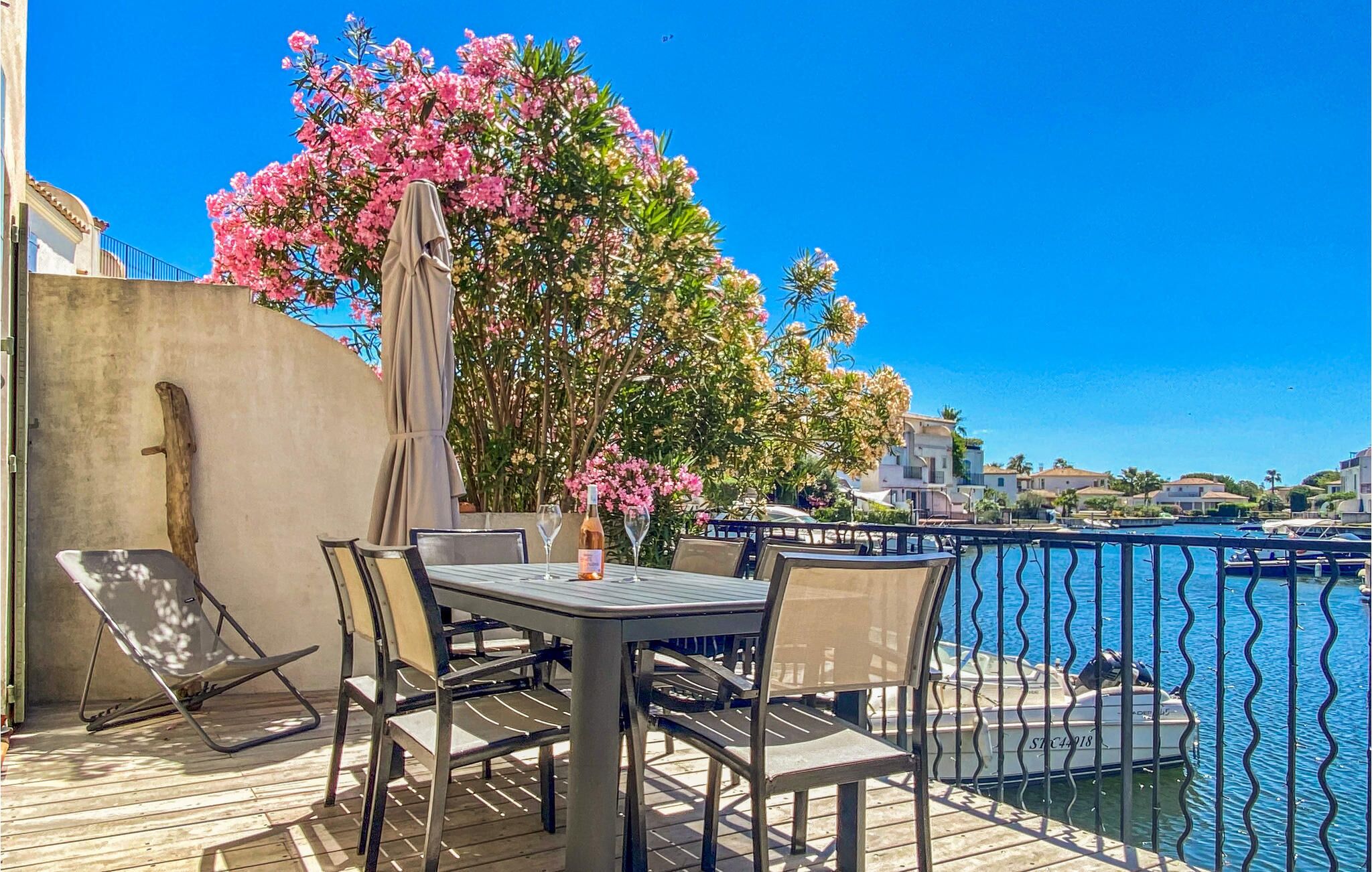 Een terras buiten met een tafel en stoelen, een bloeiende roze boom, en zicht op het water en gebouwen op de achtergrond.