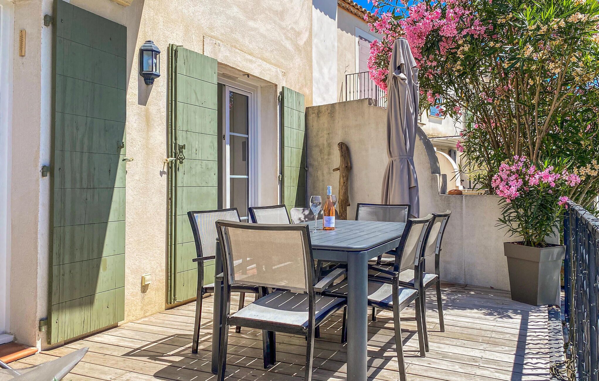 Um pátio externo com mesa, cadeiras, uma garrafa de vinho e um vaso de planta.
