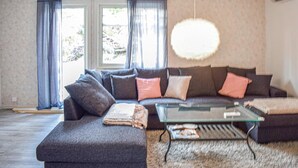 A living room with a dark grey sofa, multiple cushions, a glass coffee table, and a fluffy rug. - 2 bedroom nice home in Figeholm (Figeholm)