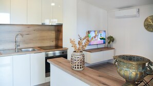 Una cocina moderna con armarios blancos, encimera de madera, un fregadero, lavavajillas, un jarrón decorativo, un televisor y una olla metálica decorativa.