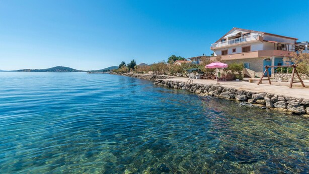 Una propiedad costera con vista despejada al mar, un espigón de piedra y un edificio con balcón.