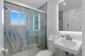 A modern bathroom with a glass-enclosed shower, a toilet, and a sink.