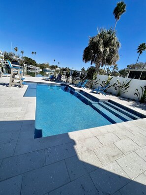 A swimming pool with clear blue water, surrounded by lounge chairs and palm trees.