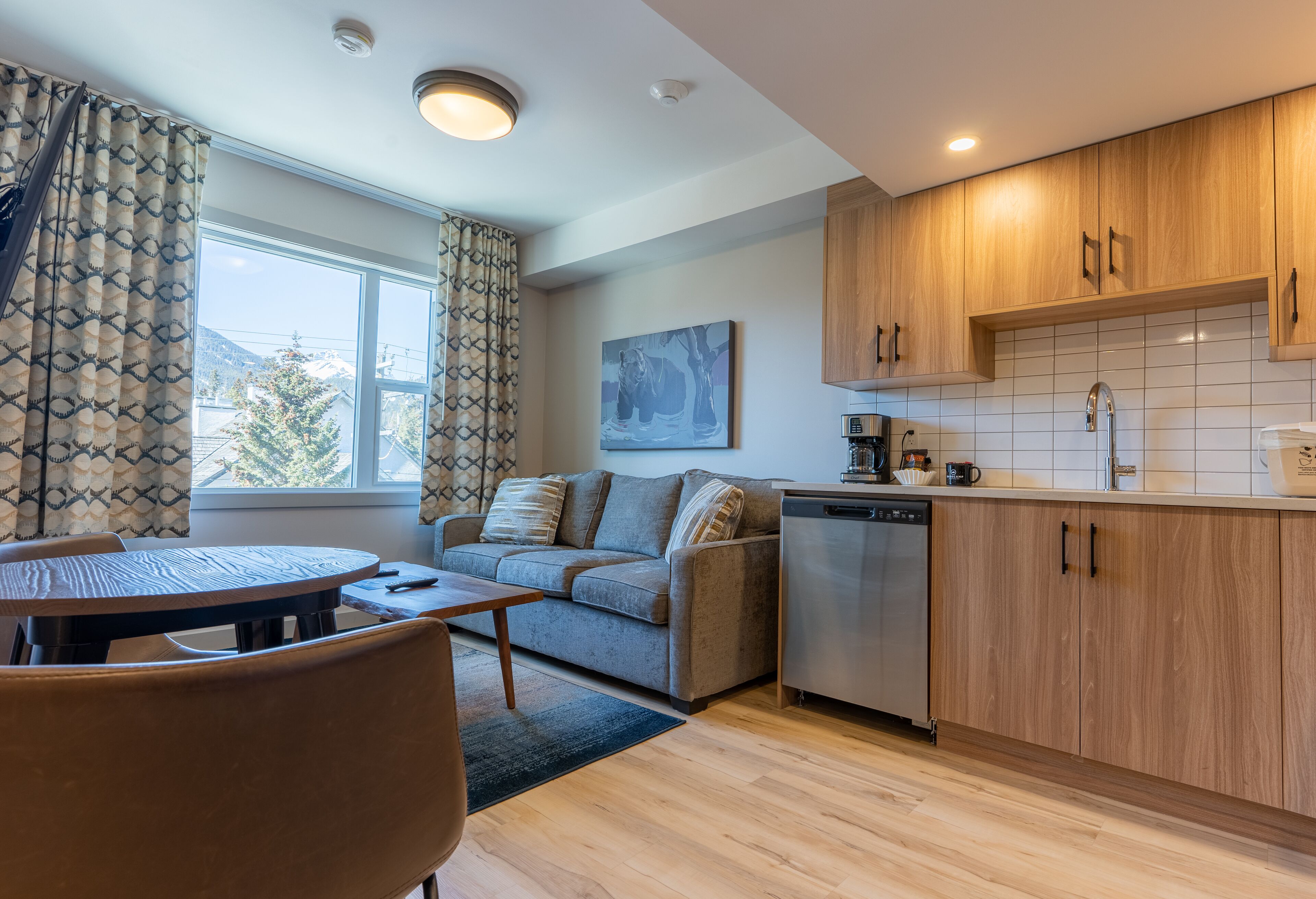 A modern kitchen with wooden cabinets, a dishwasher, and a window with curtains.