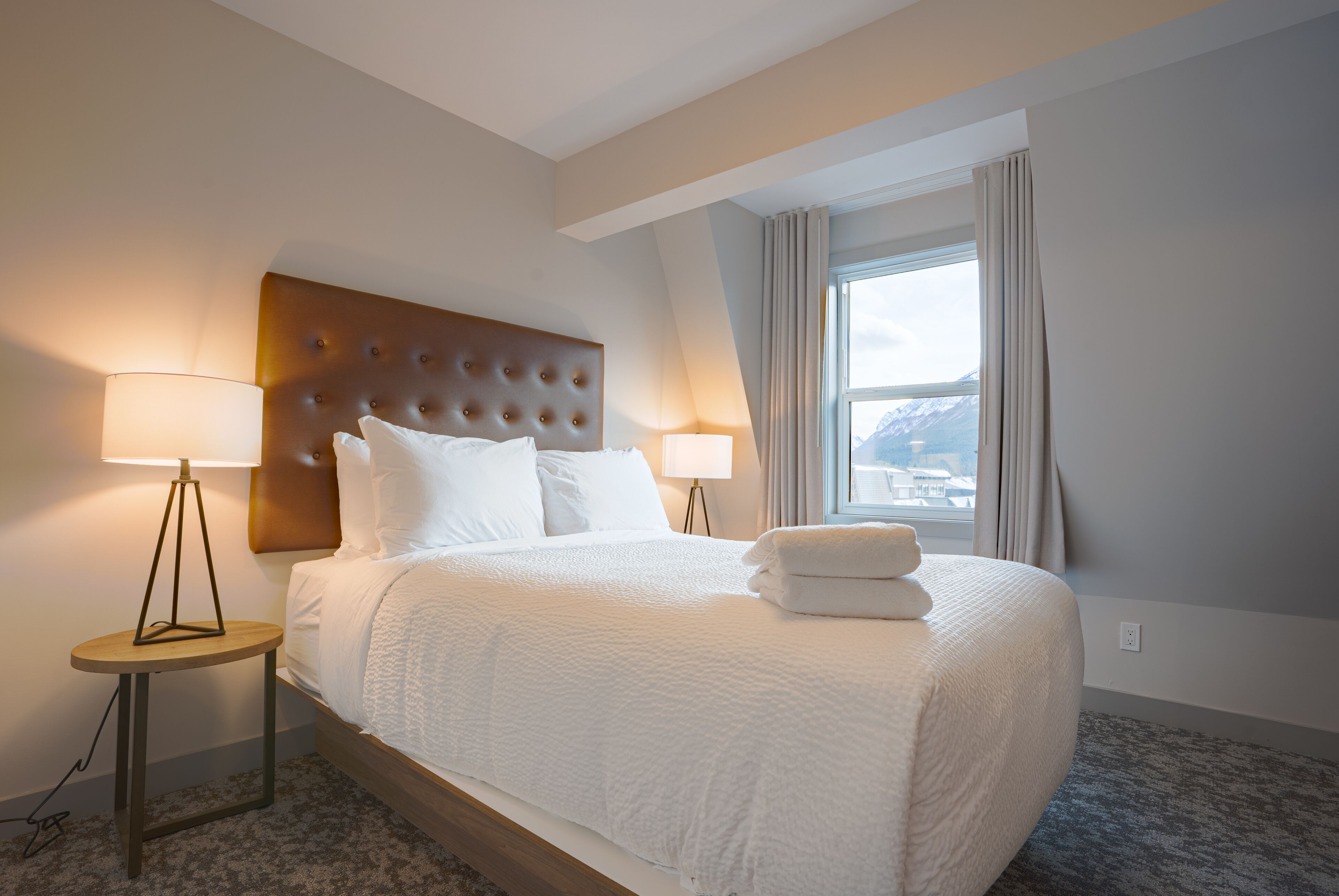 Ett hotellrum med en stor säng, två sänglampor, utsikt över bergen genom fönstret och en modern sänggavel.