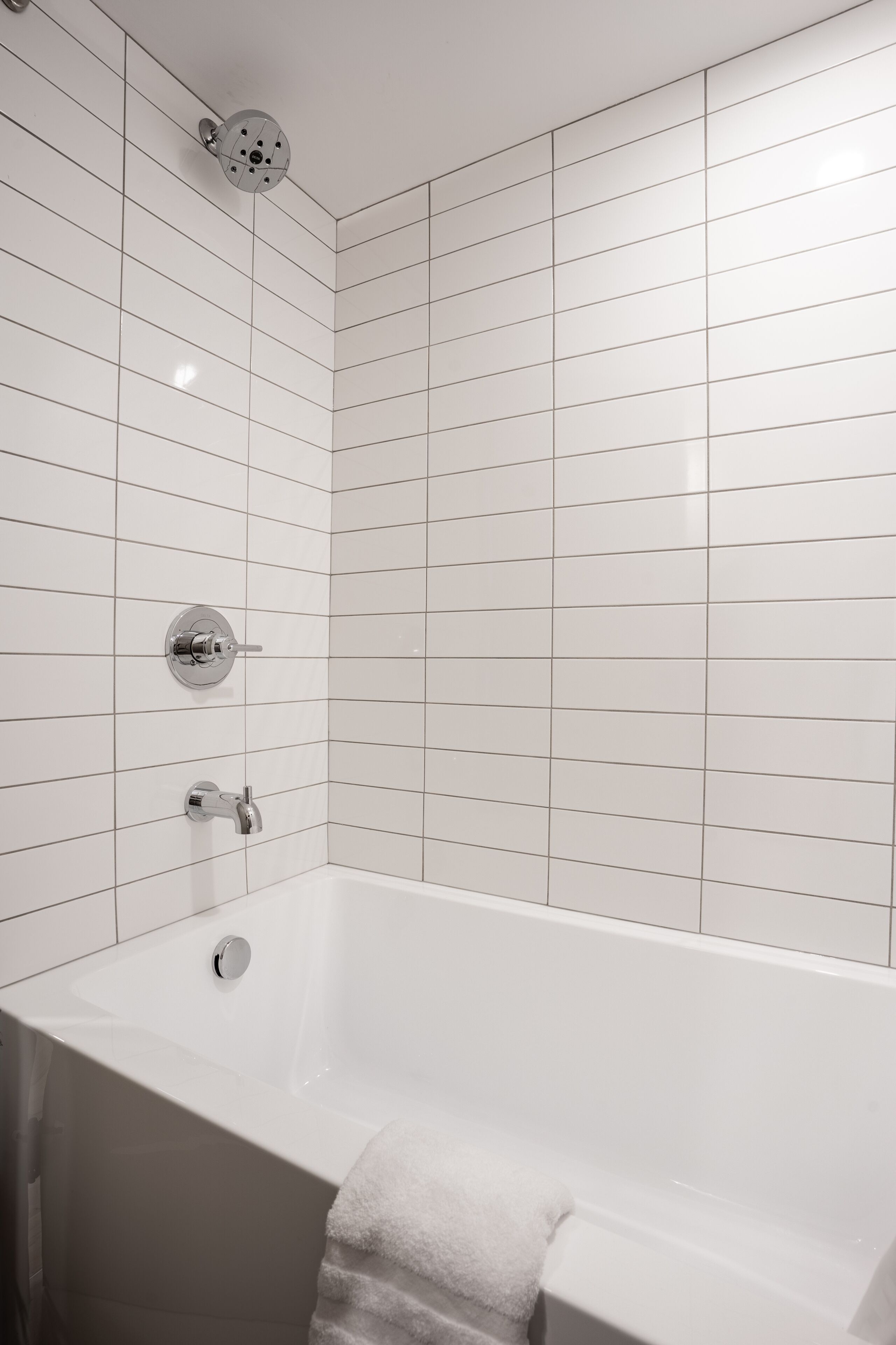 Un baño moderno con paredes de azulejos blancos, una bañera y un cabezal de ducha.