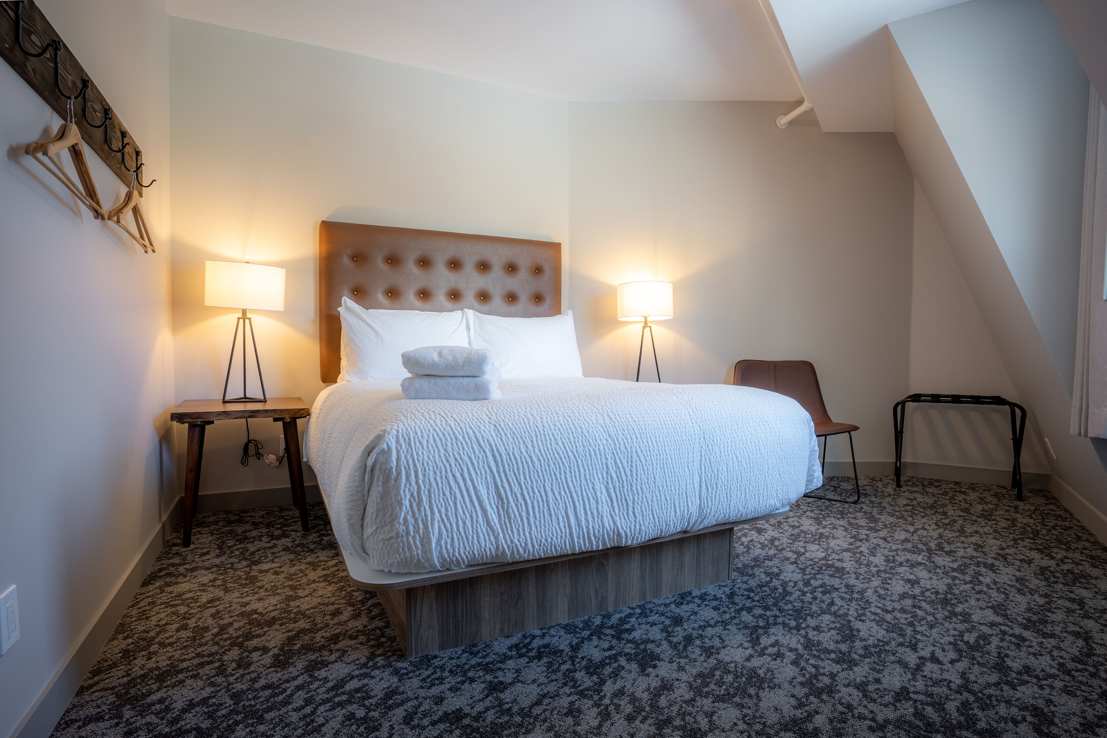 A neatly arranged hotel room with a large bed, two bedside tables, a chair, and a lamp.