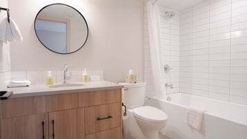 Une salle de bain moderne avec un meuble-lavabo en bois, un miroir rond, des toilettes et une baignoire dotée d’un rideau de douche.