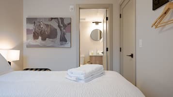 A hotel room with a bed, a painting of a bear, a round mirror, and a wooden hanger on the wall.