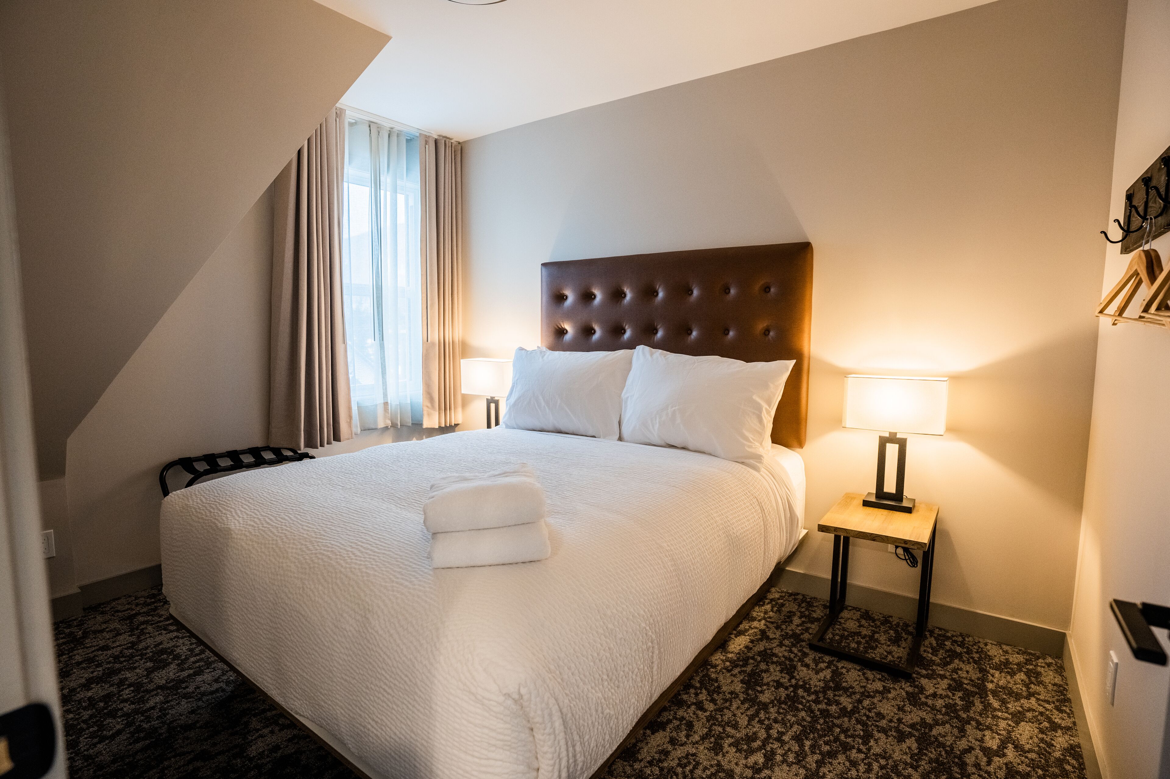 A hotel room with a large bed, two bedside lamps, a headboard, and a window with curtains.