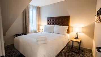 A hotel room with a large bed, two bedside lamps, a headboard, and a window with curtains.